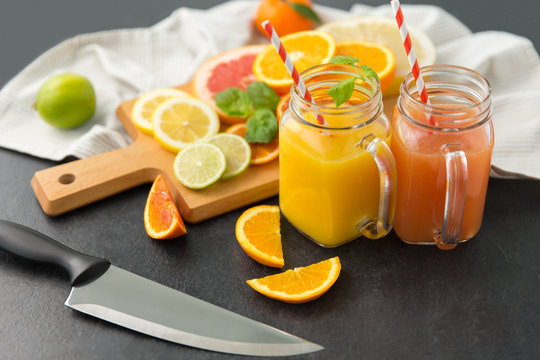 food , healthy eating and vegetarian concept - mason jar glasses with juice and citrus fruits on slate table top