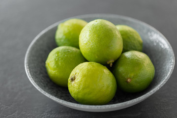 food, healthy eating and vegetarian concept - close up of whole limes in bowl on slate table top