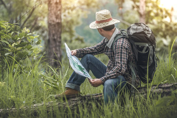 hiker sitting and look at sunset with map and checking in the forest on old wood