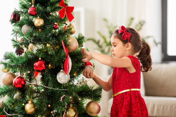 winter holidays and people concept - happy little girl decorating christmas tree at home