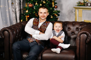 Father and son are sitting on the couch near the Christmas tree