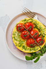 Frittata with arugula, potatoes and cherry tomatoes in iron pan on old stone table background. Top view.