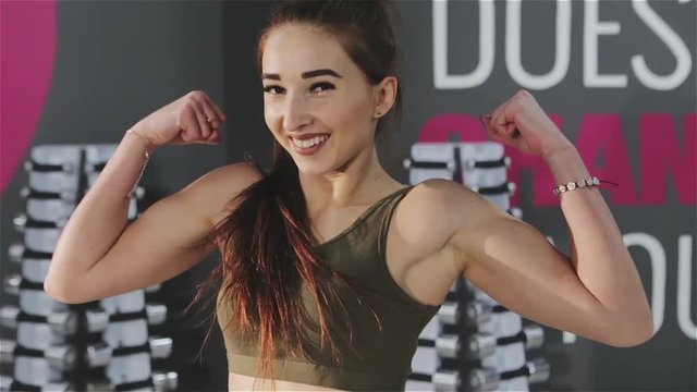 Fit girl or fitness trainer smiling and showing her biceps.