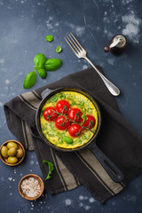 Frittata with arugula, potatoes and cherry tomatoes in iron pan on old stone table background. Top view.