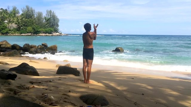White man alone doing eastern healing physical practice Chinese chi kung exercises standing on beach. Yoga teacher demonstrates professional poses quigong summer nature background. Health cardio care