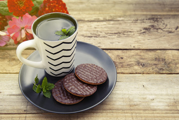 Chocolate cookies with a cup of tea on old wooden background. Knitted fabric. Copy space.