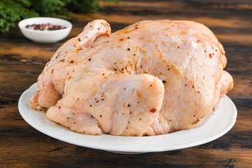 Uncooked whole chicken marinated with spices on white plate