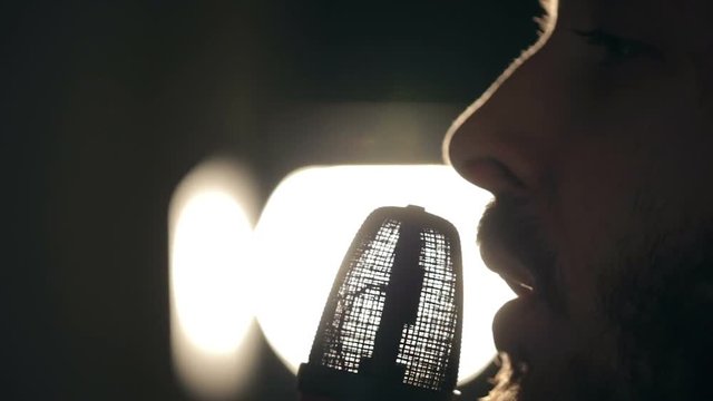 Close up shot of singer in the studio. Close up shot of microphone and man's face. Shot in counterlight