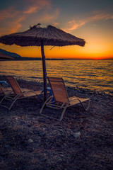 Sun beds on a rocky beach at sunset with a straw umbrella perfect for tourists on the Island of Samothrace in Greece