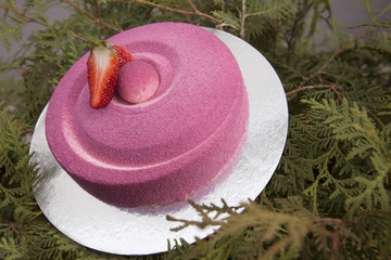 Homemade round pink cake with strawberries on a silver plate on a green background