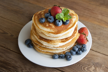 American pancakes with strawberry and blueberry jam, delicious dessert for breakfast, rustic style, wooden background. Copy space.