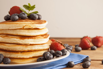 American pancakes or fritters served with strawberry and blueberry jam, delicious dessert for breakfast, rustic style, wooden background.