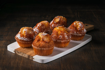 Freshly baked vanilla muffins with sugar powder, served on wooden board. Horizontal. Copy space, Dark Background.