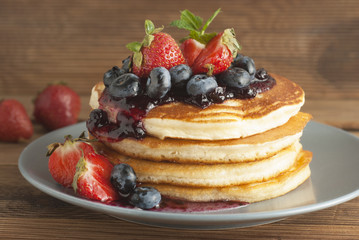 American pancakes or fritters served with strawberry and blueberry jam, delicious dessert for breakfast, rustic style, wooden background.