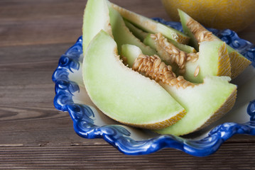 Cantaloupe yellow fresh melon isolated with sliced melon, in beautiful vintage blue plate, wooden table background. Summer fruits.