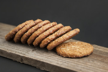 Oatmeal cookies or biscuits with oats, nuts, eggs and flour on brown dark woodenboard with black background, side view.