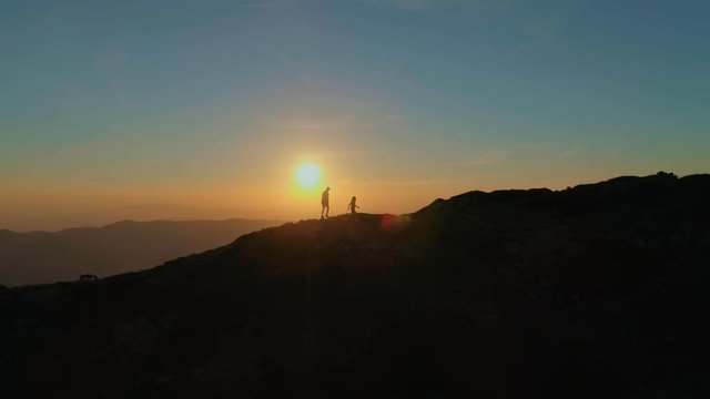 Amazing and inspiring romantic sunset over high mountains. Two people hike and camp, walk on crest edge of mountain peak, reaching goal or finish line. Motivational moment for achievements