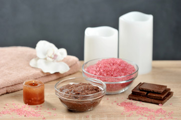 Set for spa treatments. Chocolate body scrub, chocolate bath salt, towel. The composition is complemented by candles and pieces of dark chocolate. Light background. Close-up.