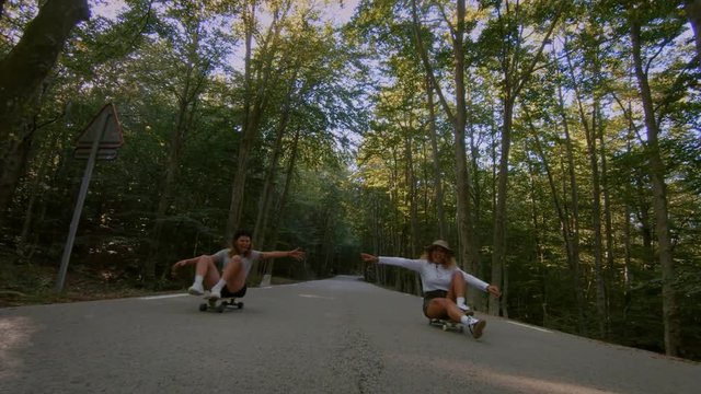 Funny and cute video of two girls laughing and smiling, having best times of lives, riding sitting on top of skateboard or longboard, cool teenagers hang out