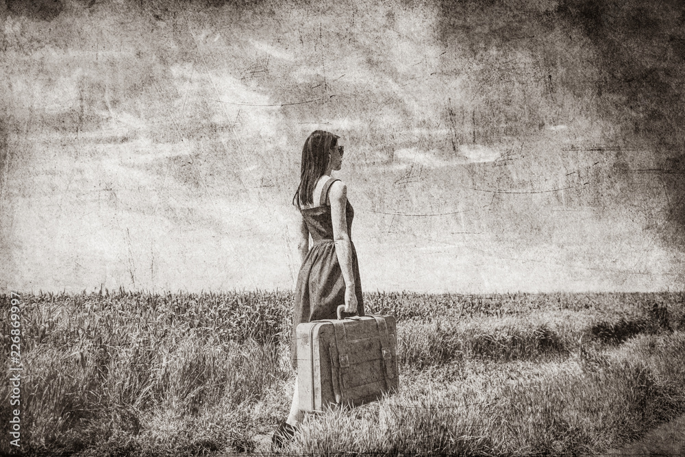 Wall mural photo of young beautiful woman with suitcase in the field. image in black and white color style