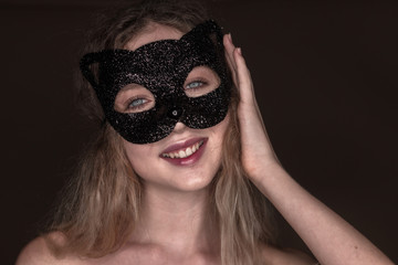 Tender cheerful happy woman posing isolated over dark beige chocolate brown background wall wearing carnival cat masquerade mask looking camera.