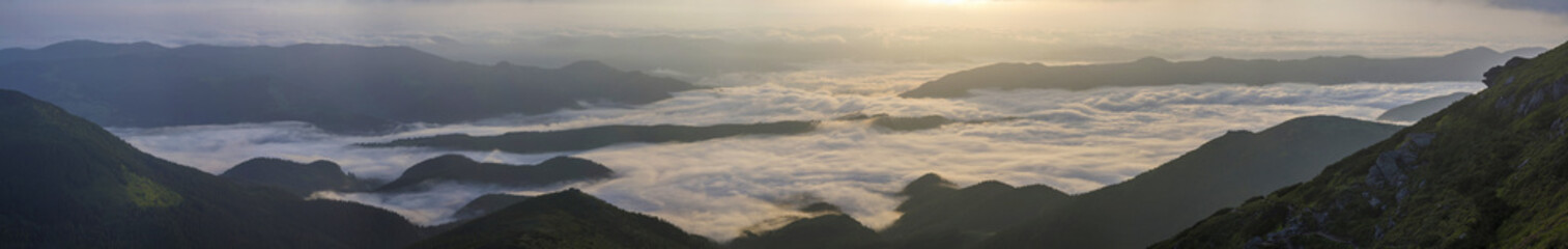 Fantastic view of mountain valley covered with low white puffy like snow clouds stretching to foggy...