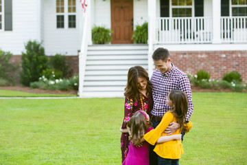 Family of Four hugging Outside their New Construction Home Farm House