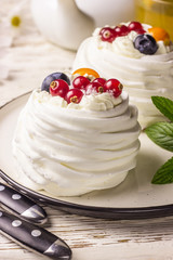 Delicious mini Pavlova meringue cake decorated with fresh red currant and blueberry