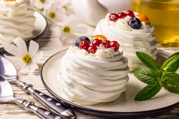 Delicious mini Pavlova meringue cake decorated with fresh red currant and blueberry