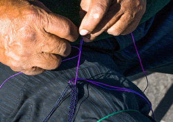 Hombre tejiendo una pulsera de hilo con su pierna