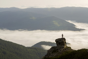 Silhouette of athletic climber tourist on high rocky formation on mountain valley filled with white...