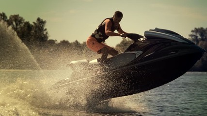 Active man riding jet ski at sunny day. Rider jumping on jet ski on waves. Sportsman having fun on jetbike in slow motion