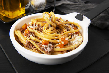 Pasta with Bolognese sauce. Parmesan and olive oil. Spaghetti is screwed onto the fork. In a white frying pan. The background is black. Italian food.