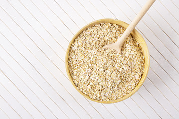 Oatmeal flakes in a wooden bowl on a white background. A wooden spoon in a bowl with porridge.