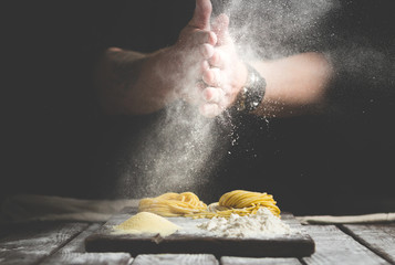 hands in flour, make homemade pasta on a table on black background