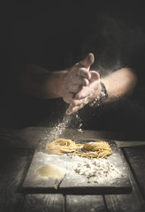 hands in flour, make homemade pasta on a table on black background