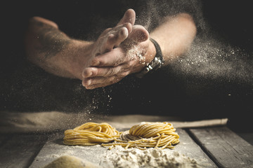 A man claps his hands and sprinkles flour on fresh pasta. Black background, rustic style