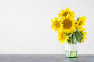 Bright yellow big sunflowers in glass vase on dark table on light texture background. Mockup banner...