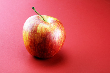 Ripe red apple with leaves on red background.