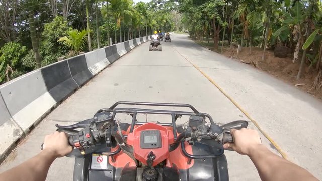 Group of people drive atvs in tropical setting, POV
