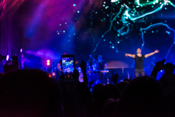 Fototapeta na wymiar Crowd at concert. People silhouettes on backlit by bright blue and purple stage lights. Cheering crowd in colorful stage lights. Raised hands and smartphones against scene