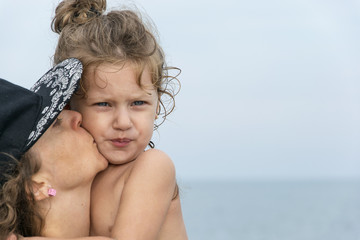 Picture of a cute little girl, being kissed by her mother on the beach 