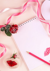 Blank notepad, pencil, rose flower, pink ribbon and lips. Concept of holiday or greetings. Selective focus, top view, flat layout.