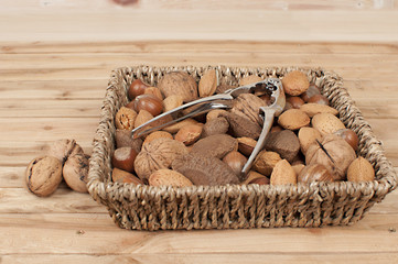 different kind of nuts in straw basket on wooden table with nutcracker