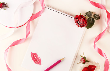 Blank notepad, pencil, rose flower, pink ribbon and lips. Concept of holiday or greetings. Selective focus, top view, flat layout.