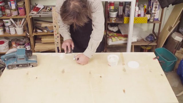 Crane shot. High angle view. Senior carpenter spackling wooden board
