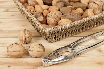 different kind of nuts in straw basket on wooden table with nutcracker