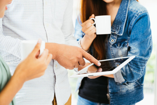 Casual businessman showing presentation on digital tablet to team while relax and drinking coffee. Business teamwork meeting. Young coworker making relax business discussion in modern office