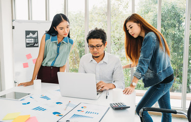 Young asian casual businessman and woman meeting in modern office. Teamwork concept. Business partner presenting working information on laptop with analysis graph documents on table