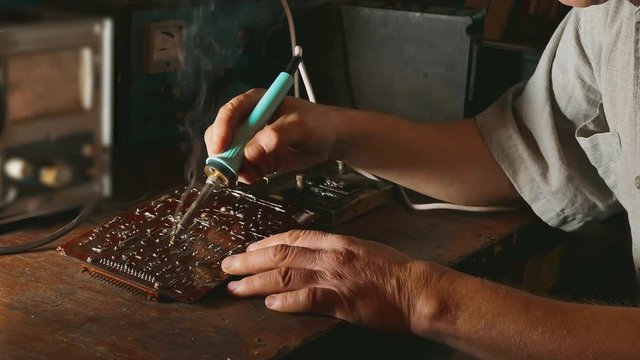 the old man repairs the chip radio technician smoke is coming repair soldering iron. Engineer or technician repair electronic circuit board with soldering iron lifestyle. man repair chips concept